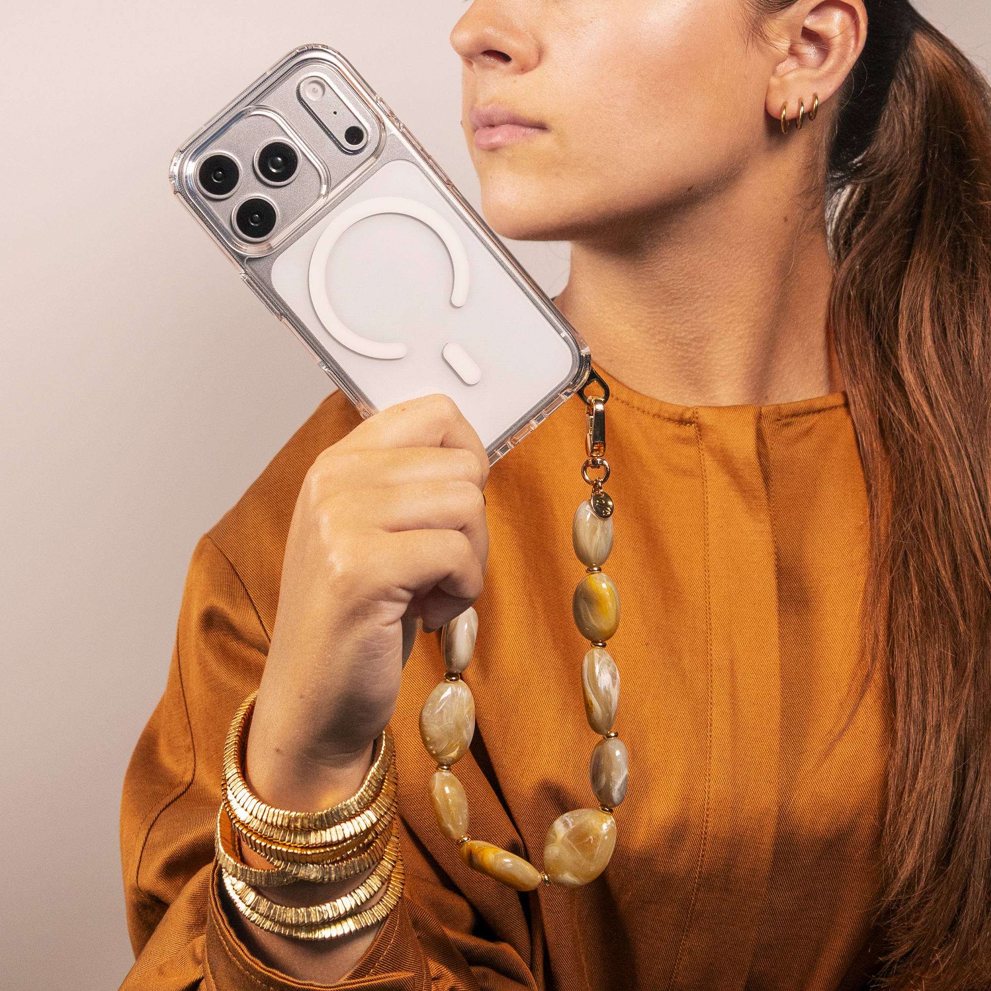Woman in mustard blouse holding a smartphone in clear case with beige beaded strap.