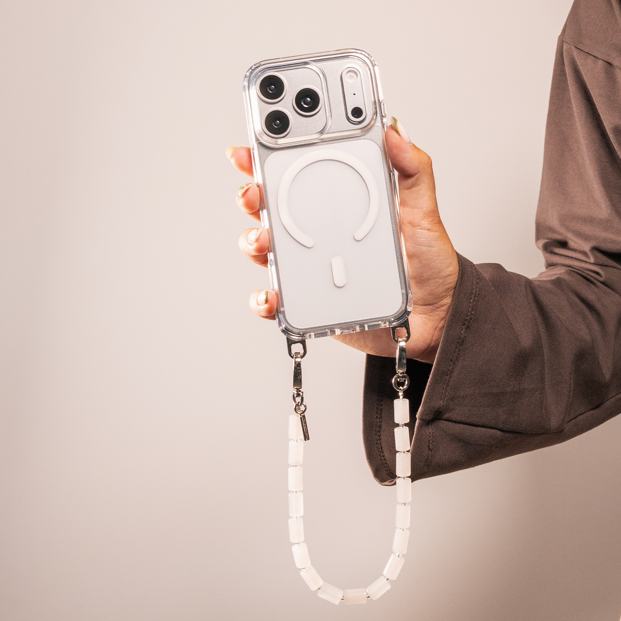 A person holds a phone in a clear case with a white bead strap against a neutral background.