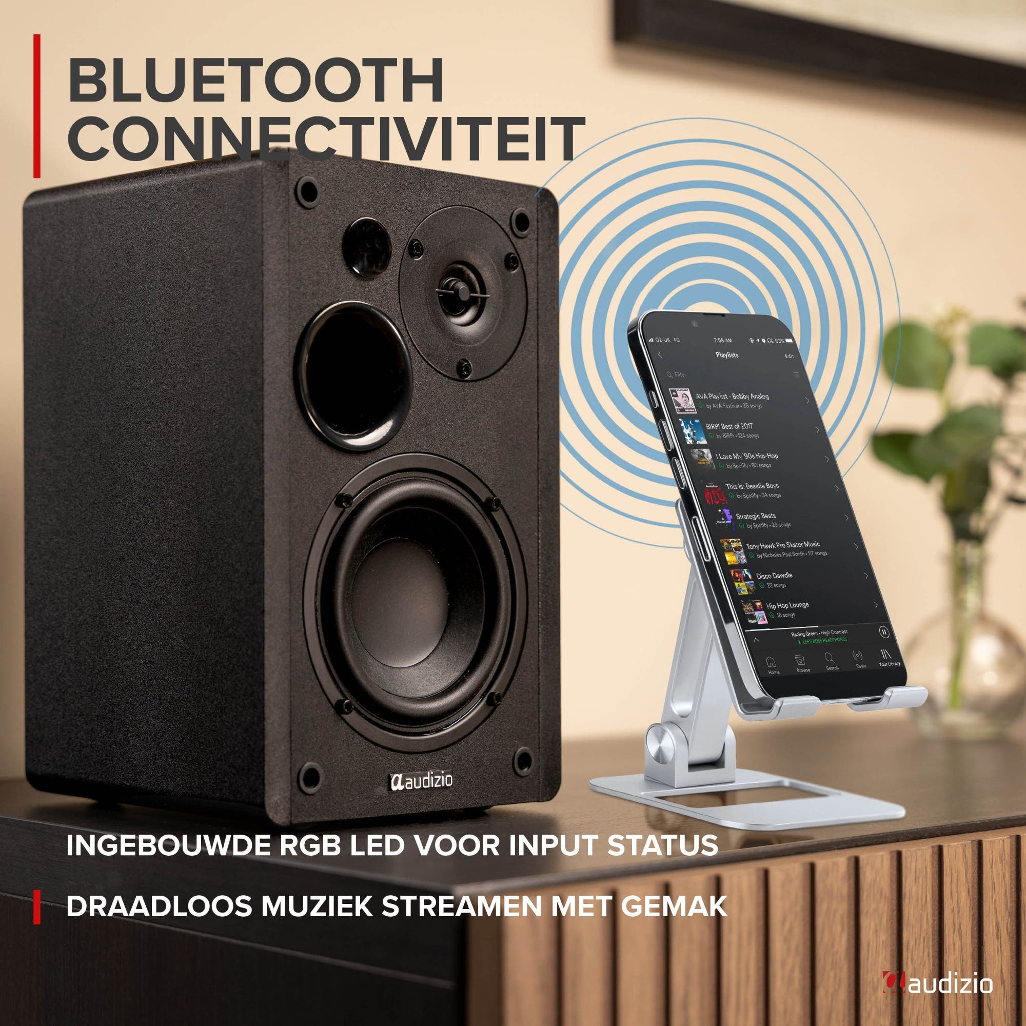 Un altavoz Audizio negro junto a un teléfono en un soporte, transmitiendo música de forma inalámbrica.