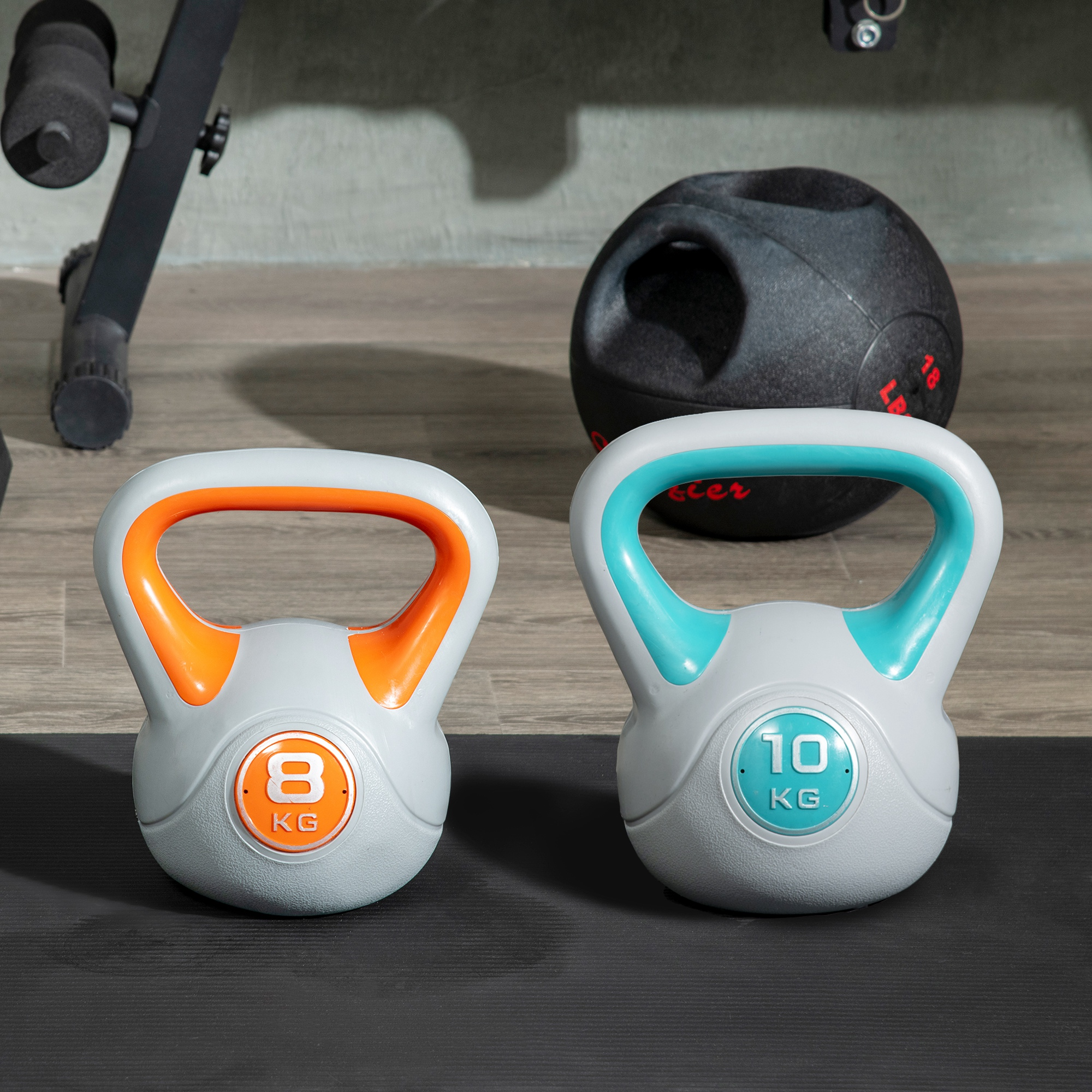 Dos pesas rusas de 8 kg y 10 kg sobre una esterilla de gimnasio con un balón medicinal al fondo.