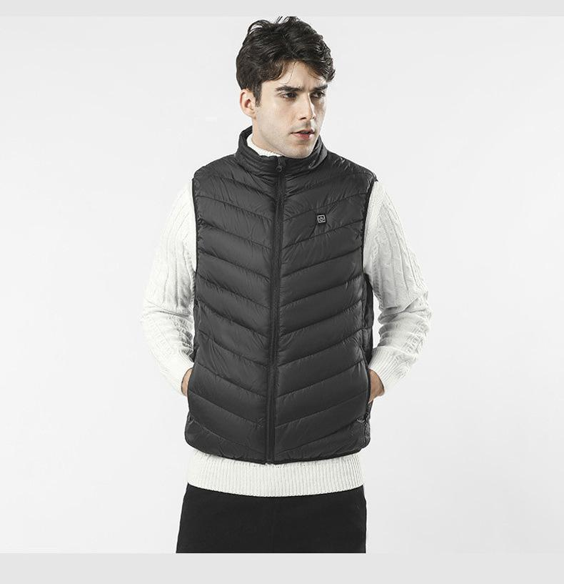 A man wears a black puffer vest over a white sweater against a white background.