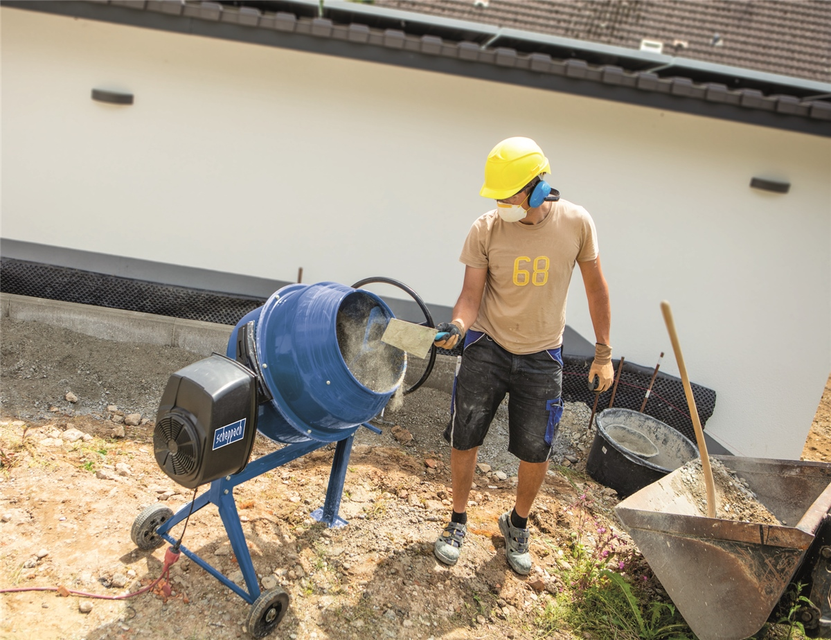 Un lavoratore con elmetto mescola cemento in una betoniera blu in un cantiere.