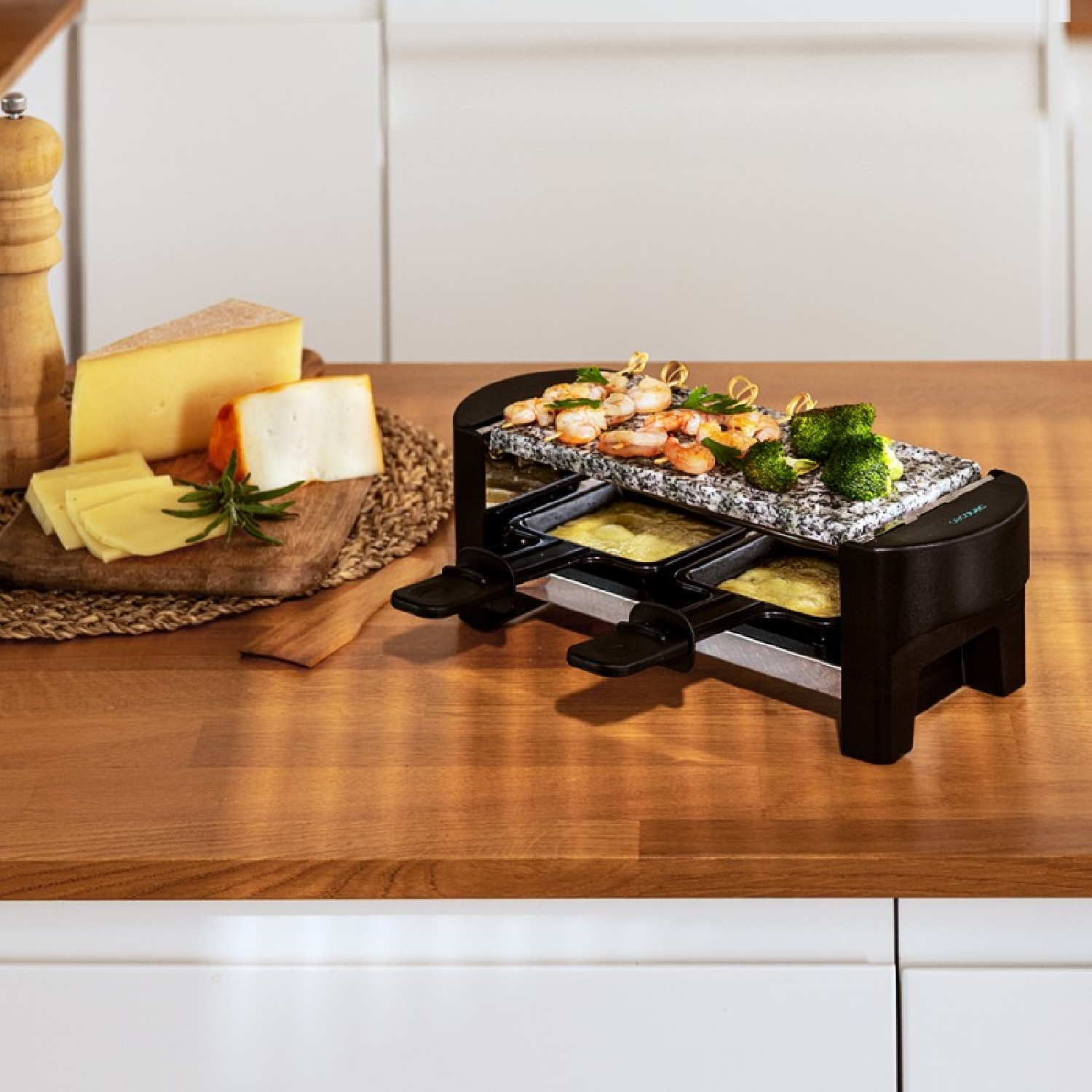 Ein Raclette-Grill auf einem Holztisch mit geschmolzenem Käse, Shrimps, Brokkoli und Käseplatten im Hintergrund.