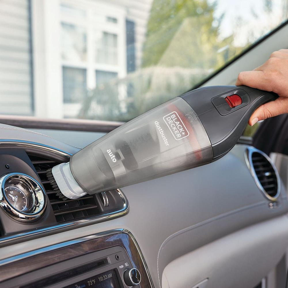 Eine Hand benutzt einen Handstaubsauger, um die Lüftungsschlitze eines Autos zu reinigen.