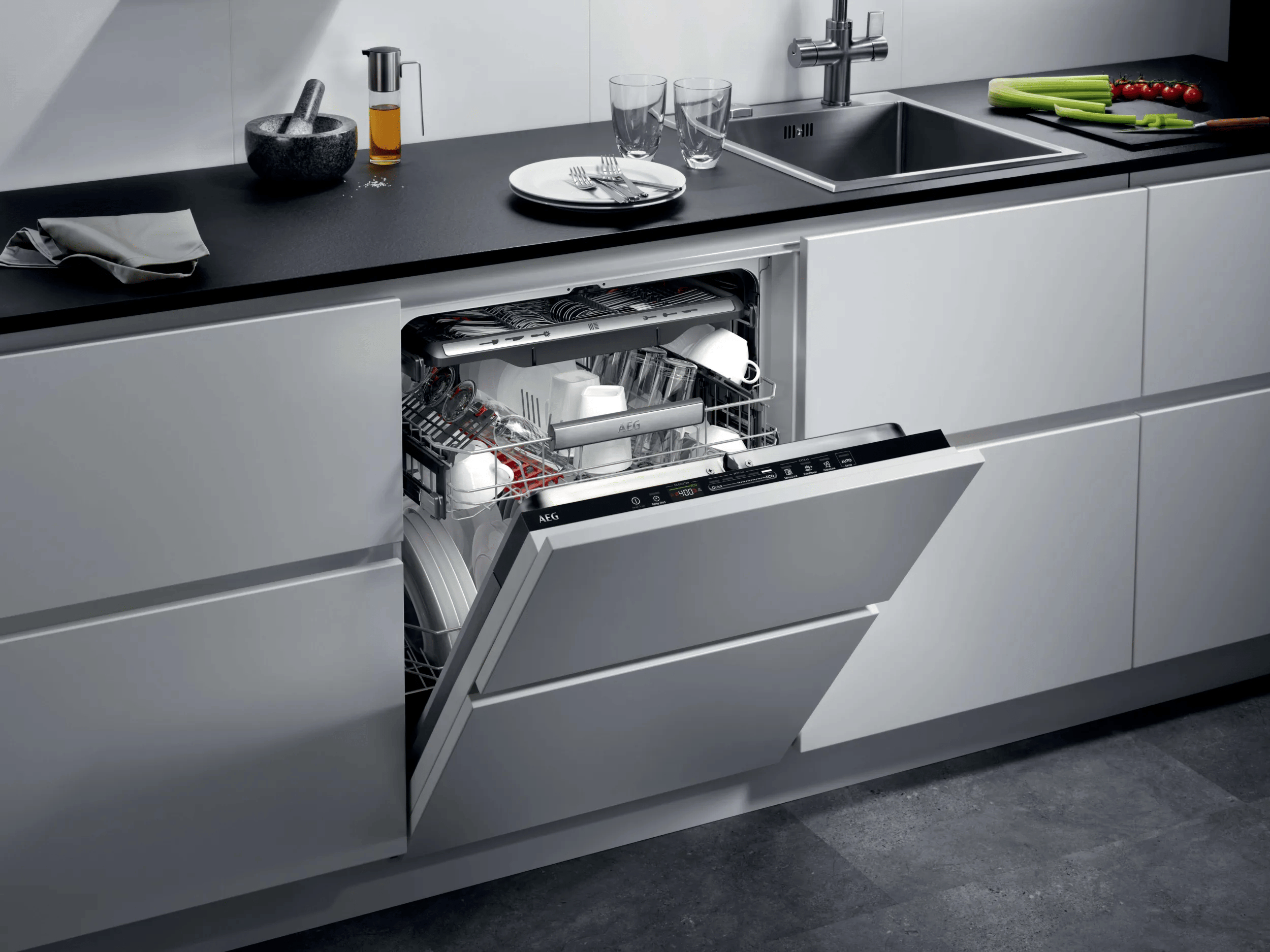 Una lavastoviglie bianca aperta in una cucina moderna con piano di lavoro nero, lavello e stoviglie.