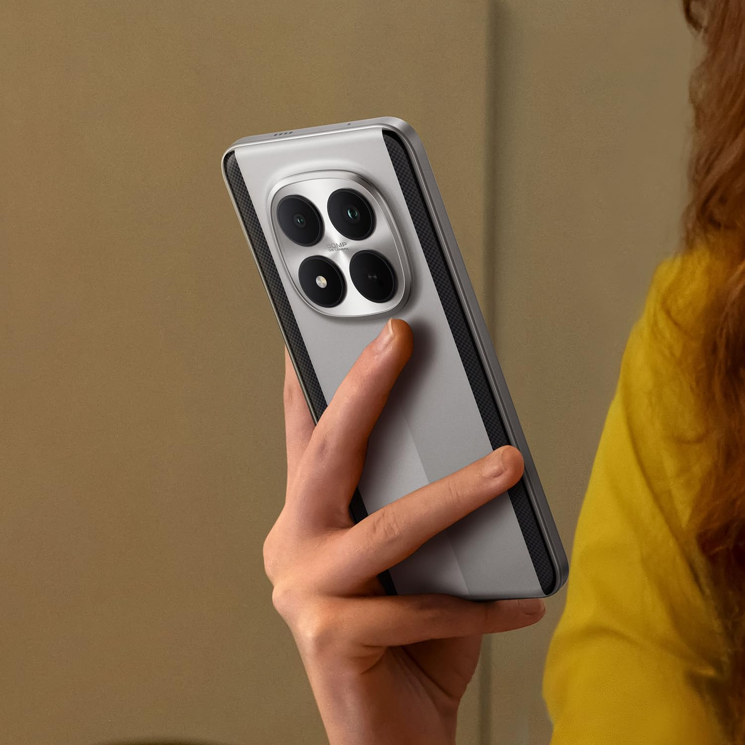 Una persona tiene in mano uno smartphone argentato con un modulo a quattro fotocamere sul retro.