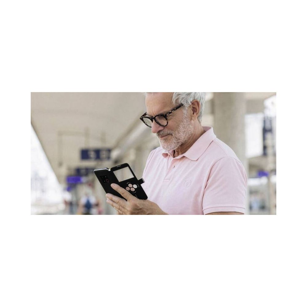 Anziano con occhiali e polo rosa tiene in mano uno smartphone aperto.