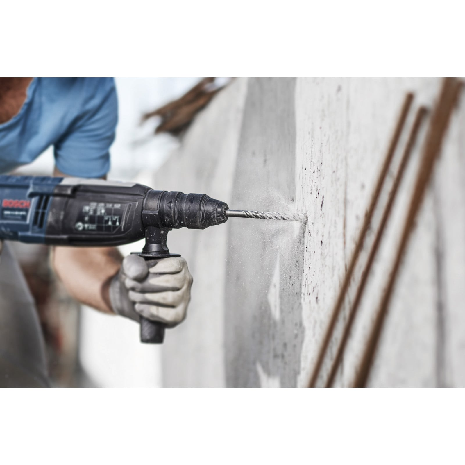 Ein Arbeiter bohrt mit einer blauen Schlagbohrmaschine in eine Betonwand.