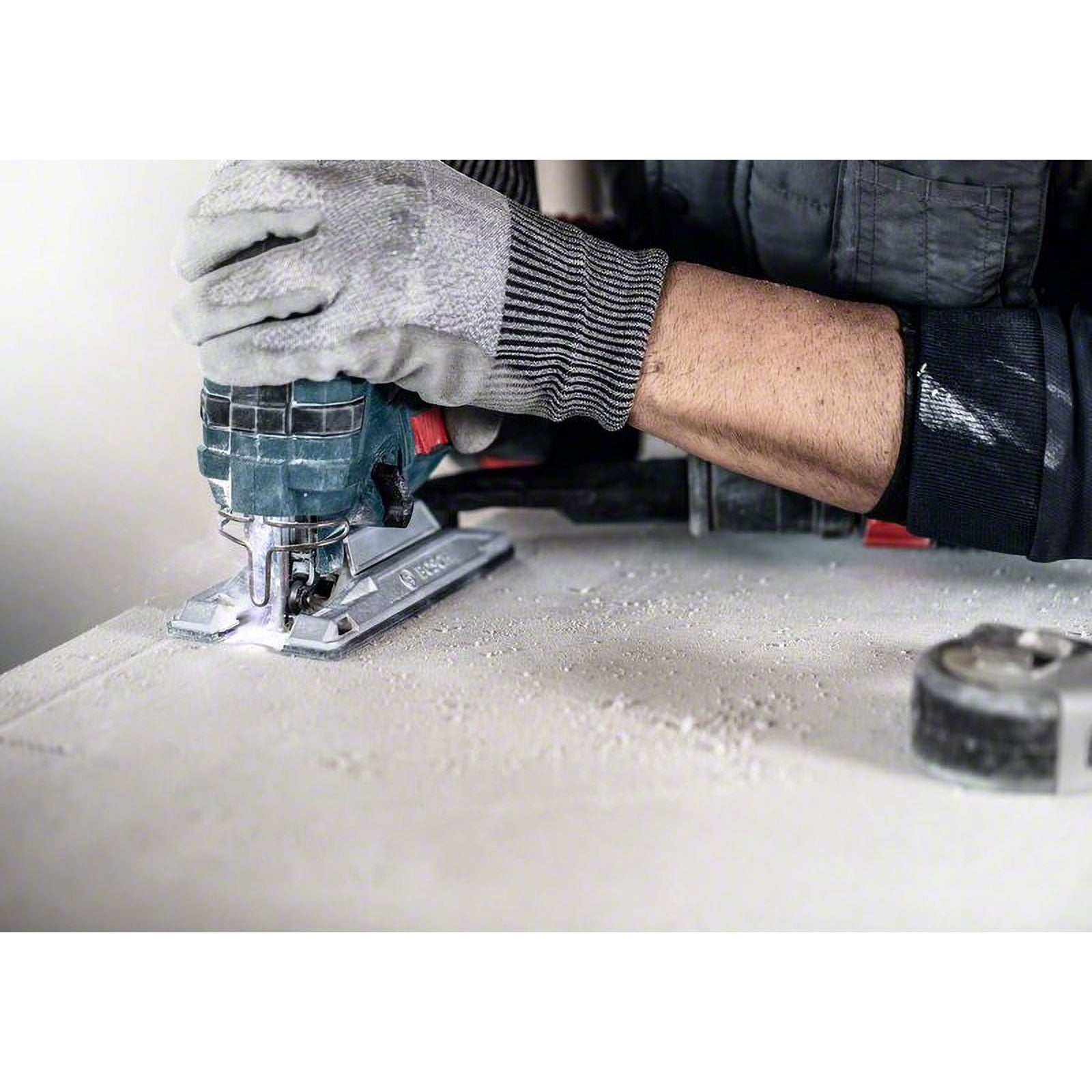 Ein Arbeiter in Schutzhandschuhen schneidet mit einer Stichsäge eine Holzplatte zu.
