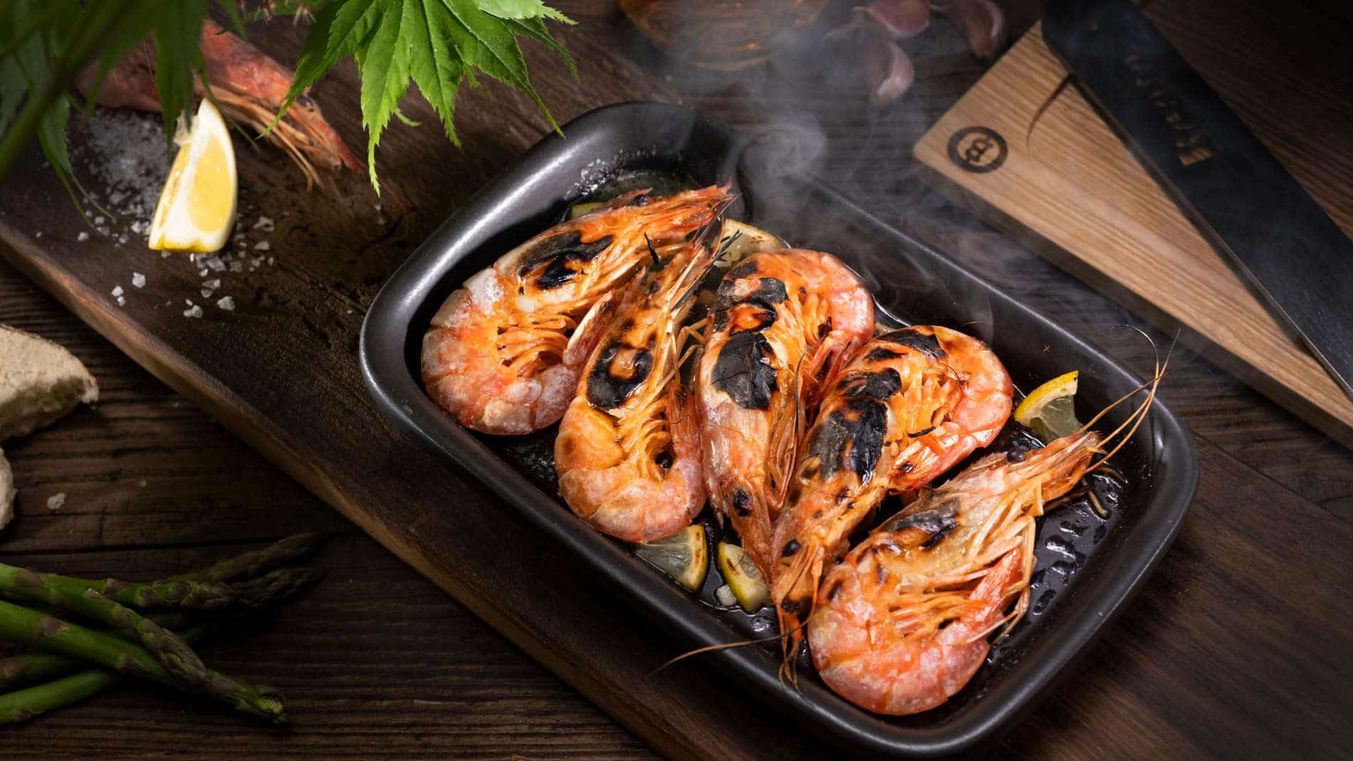 Gegrillte Garnelen dampfen in einer schwarzen Pfanne auf Holz.
