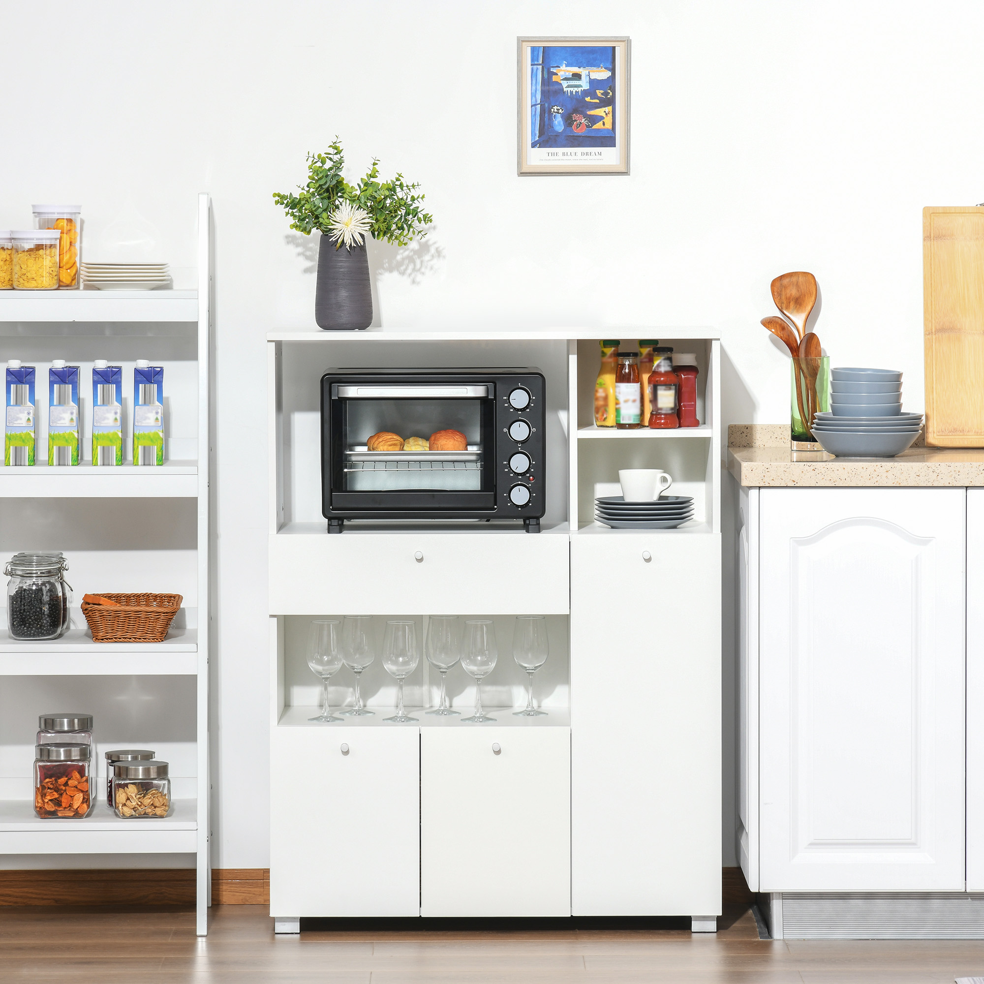 Un mueble de cocina blanco con horno negro, estantes con alimentos, copas y una encimera con platos apilados.