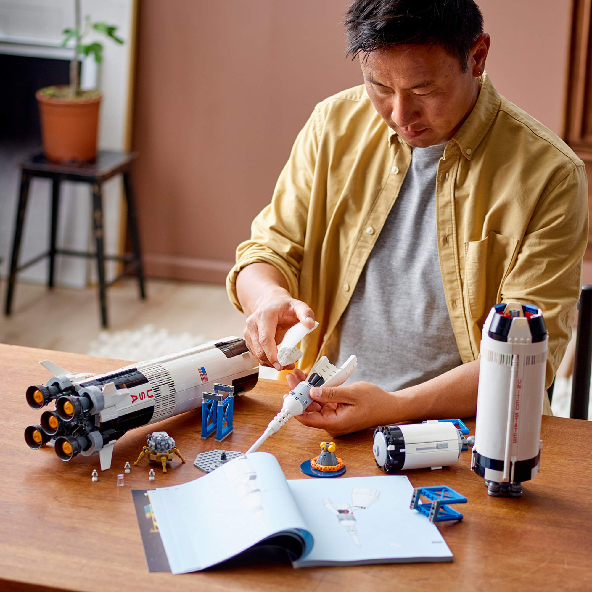 Un homme assemble un grand modèle de fusée Lego sur une table en bois.