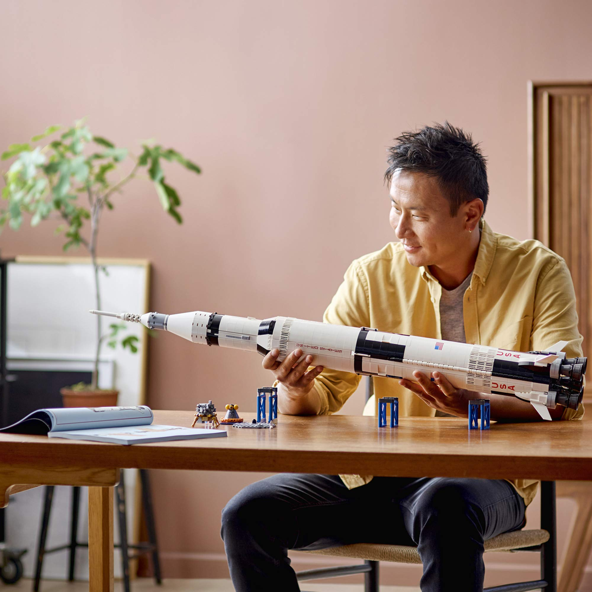 Un homme assis à une table en bois tient un grand modèle de fusée Lego.