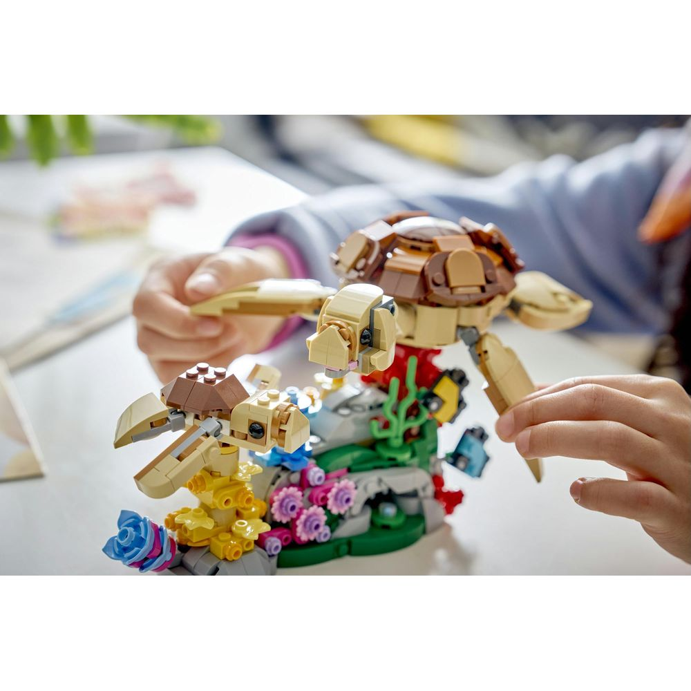 Dziecięce rączki budują kolorowy model żółwia morskiego z klocków LEGO.