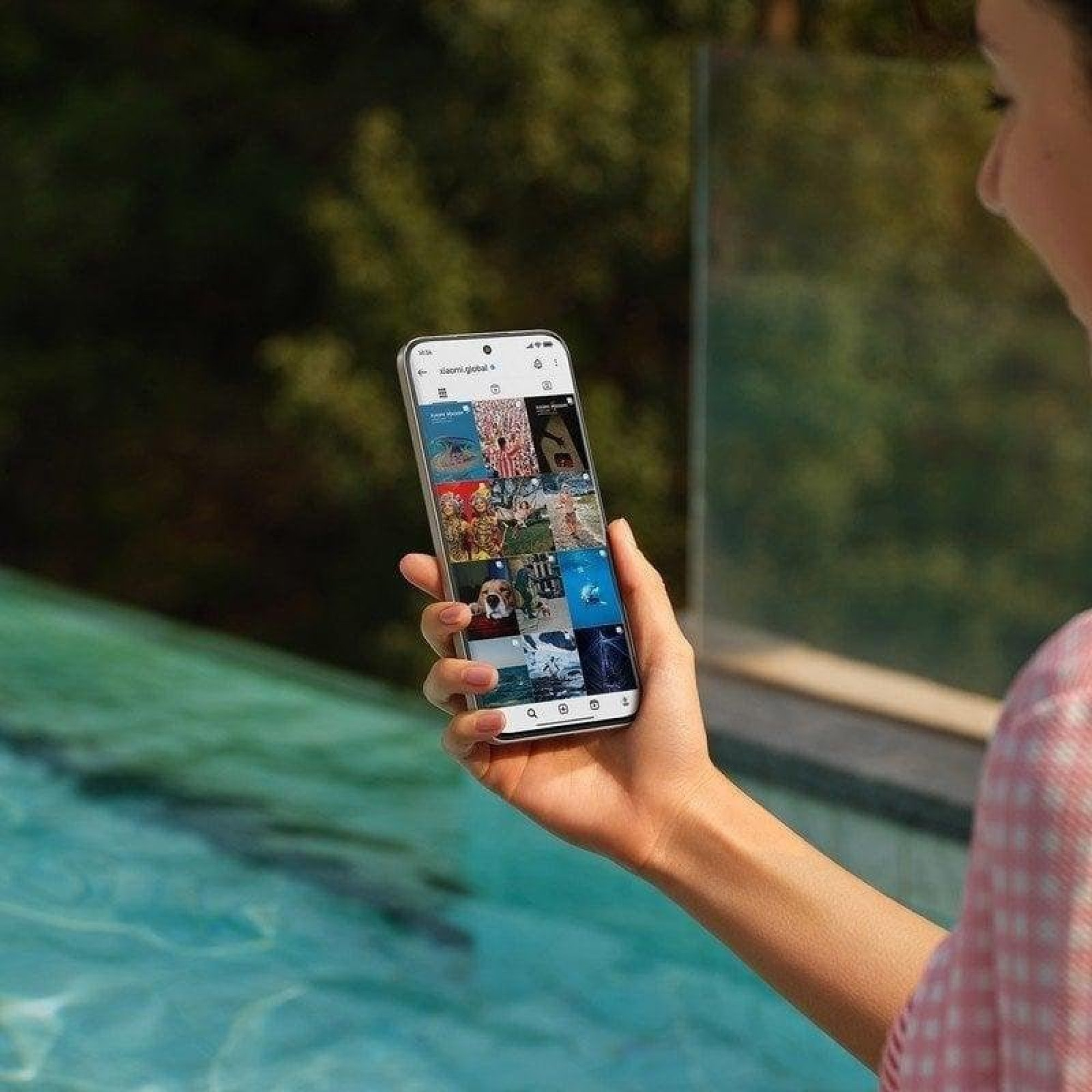 Eine Frau hält ein Smartphone mit einer Fotogalerie am Pool.