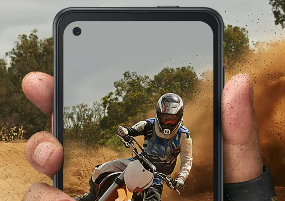Ein Smartphone zeigt einen Motocross-Fahrer, der Staub aufwirbelt, gehalten von schlammigen Händen.