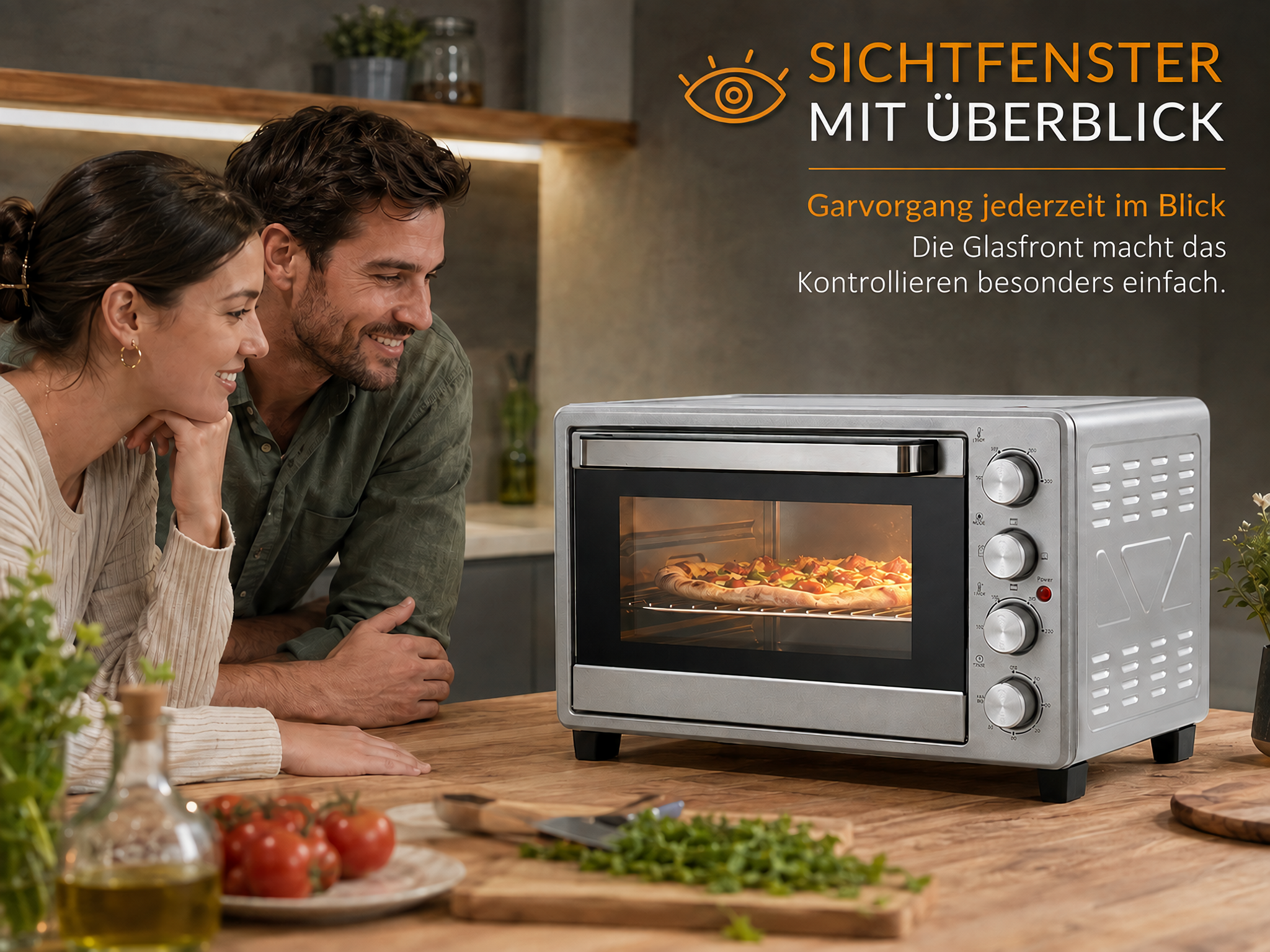 Ein lächelndes Paar beobachtet eine Pizza in einem silbernen Minibackofen.