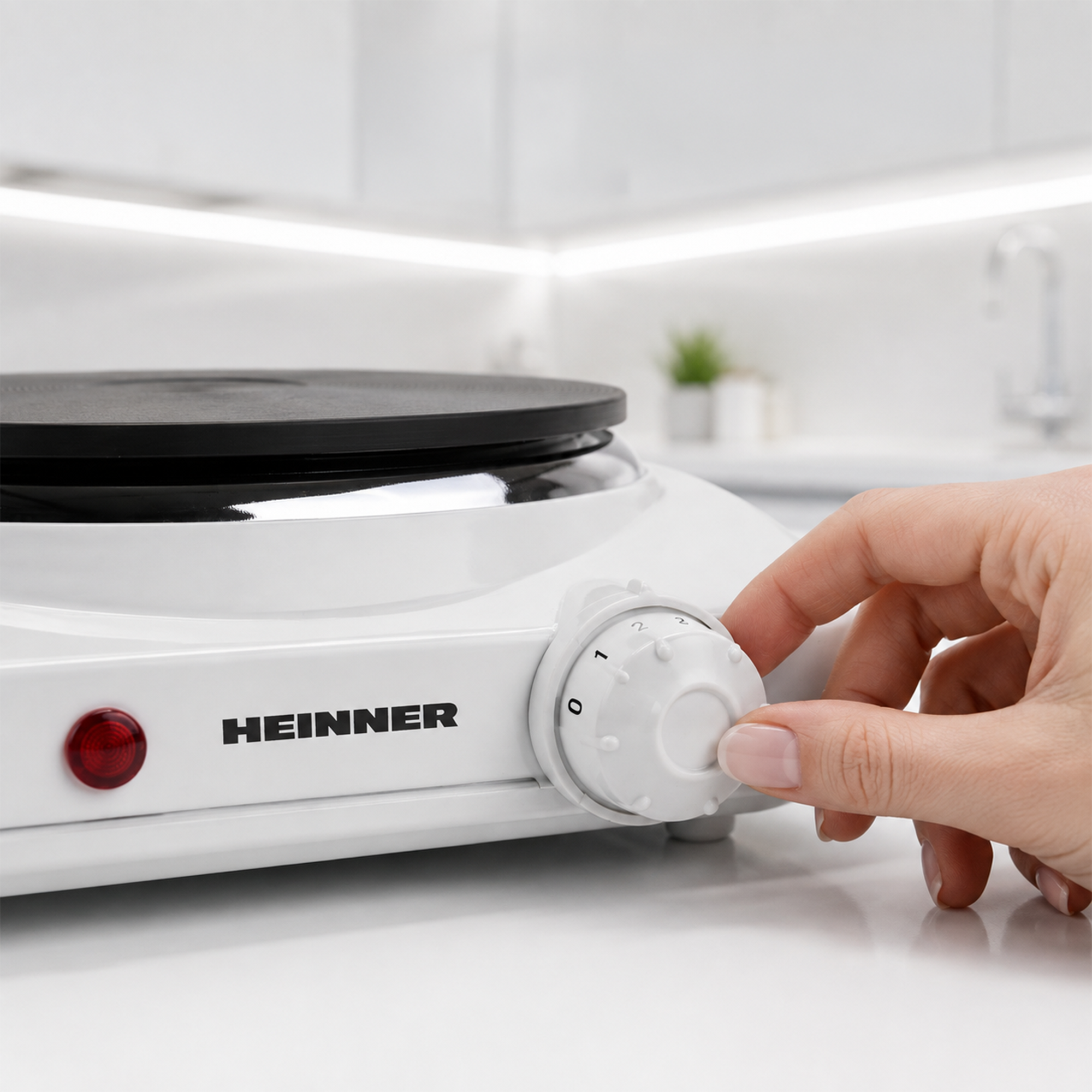 Hand stellt den Temperaturregler einer weißen Heinner-Kochplatte ein.