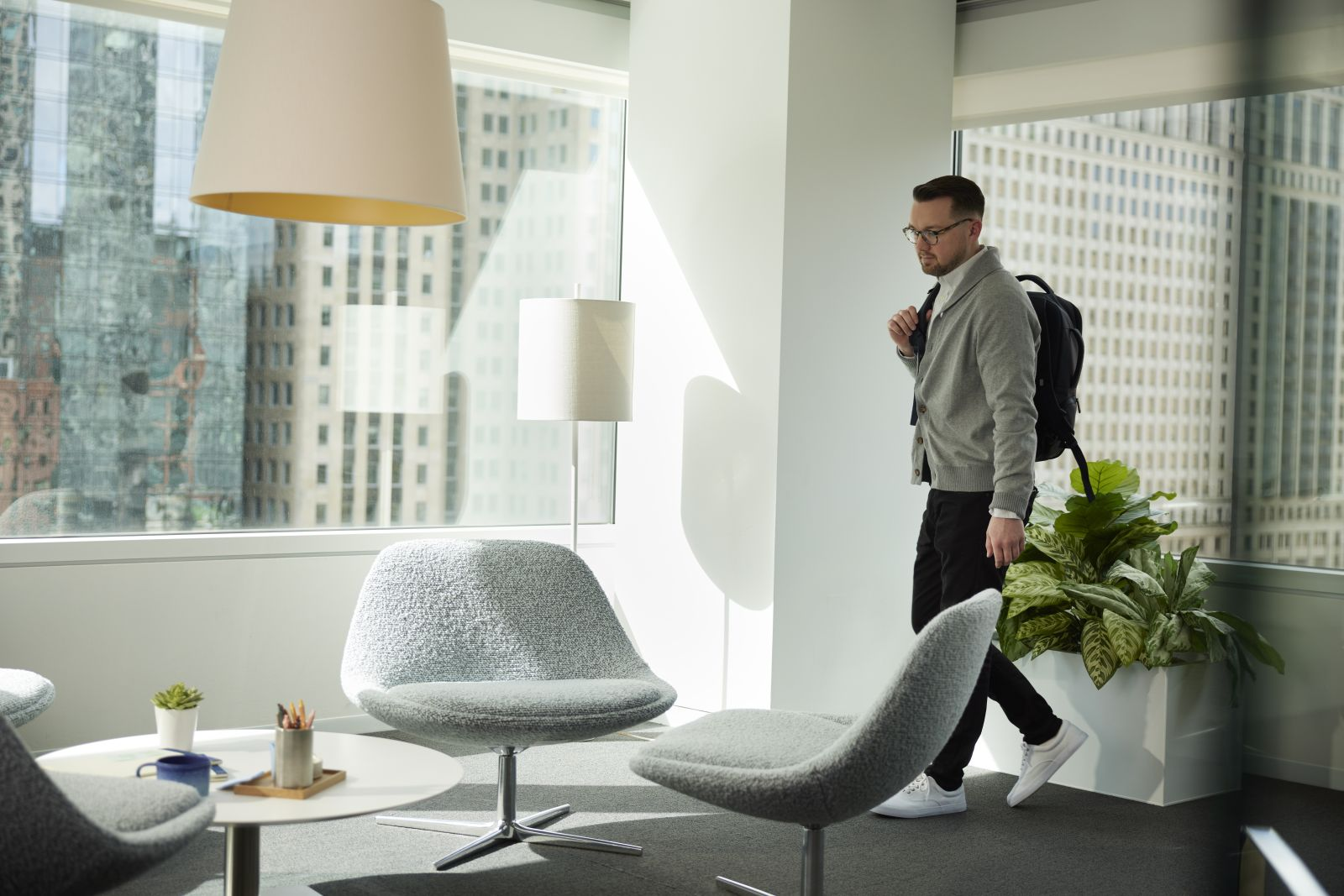 Ein Mann mit Rucksack geht durch ein modernes Büro mit großen Fenstern.