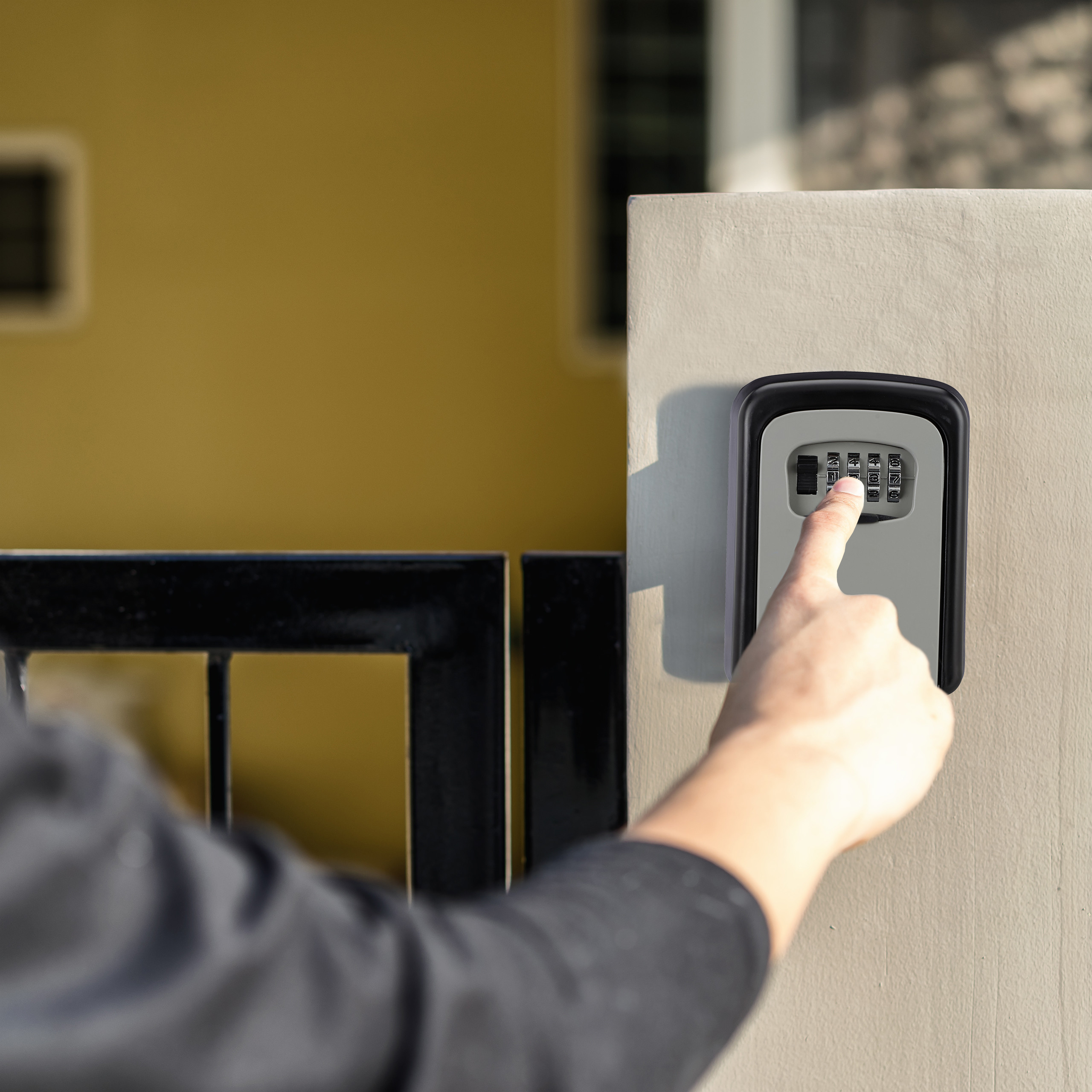 Eine Hand gibt einen Code auf einem Schlüsseltresor ein, der an einer beigen Wand befestigt ist.