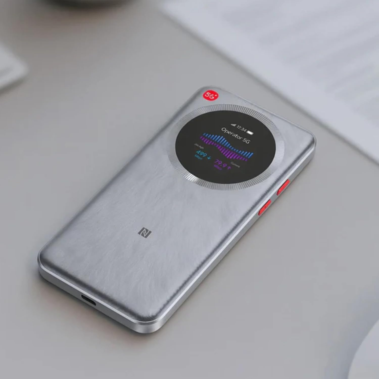 Ein silbernes 5G-Gerät mit rundem Display liegt auf einem grauen Tisch.