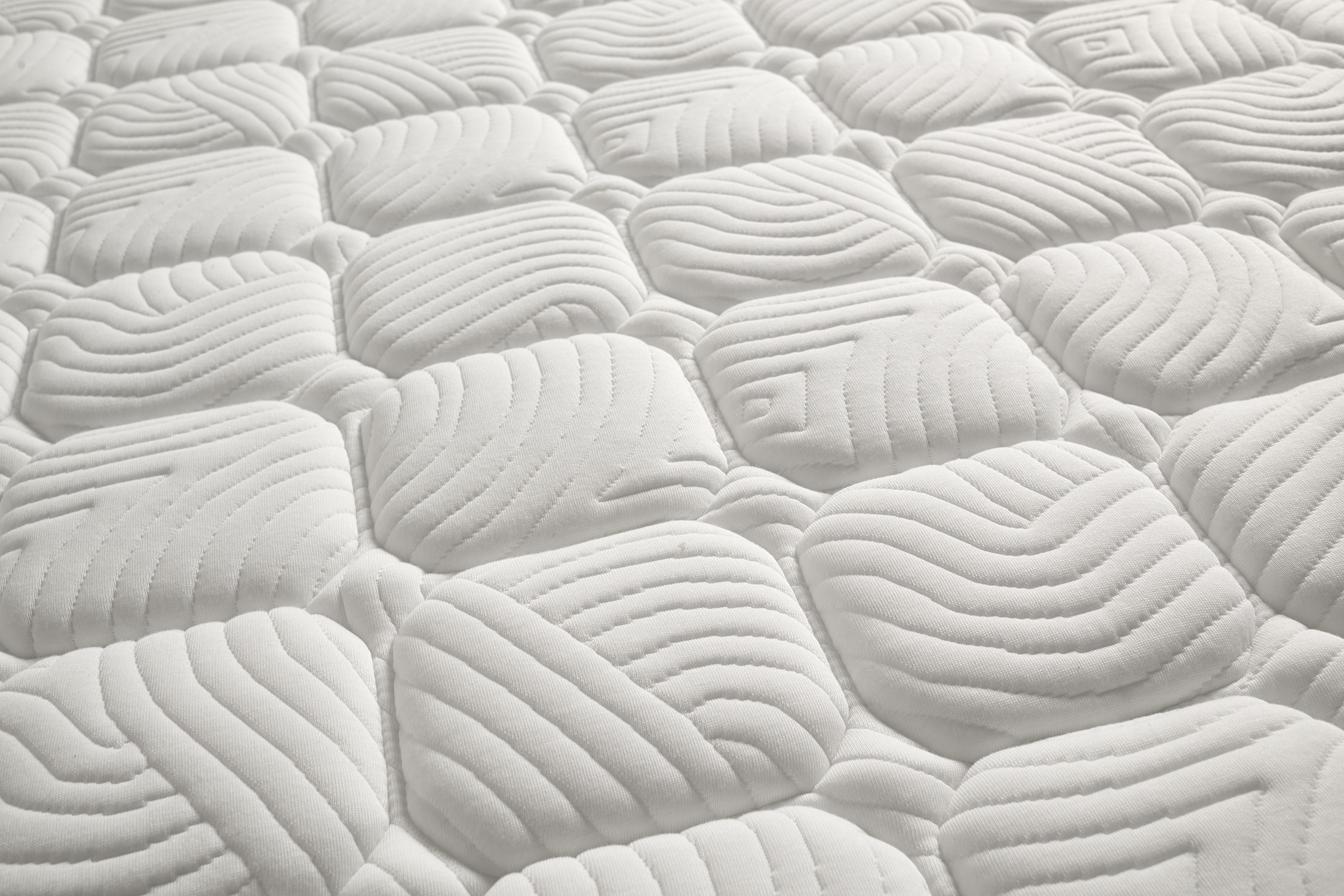 Primer plano de una superficie de colchón blanca con patrones de almohadas acolchadas y texturas onduladas.