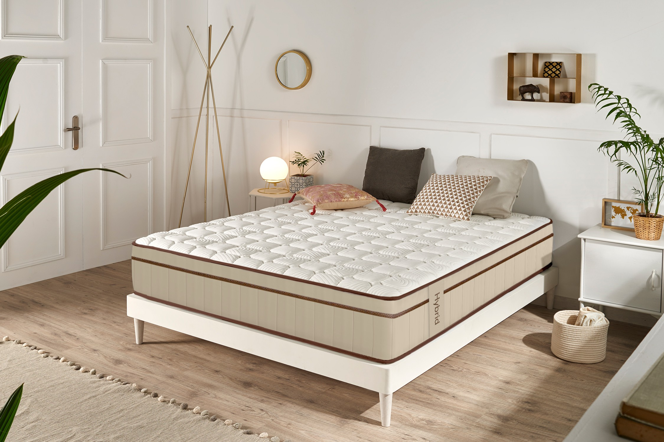 Una cama blanca con colchón beige, cojines y mesitas de noche en un dormitorio luminoso.