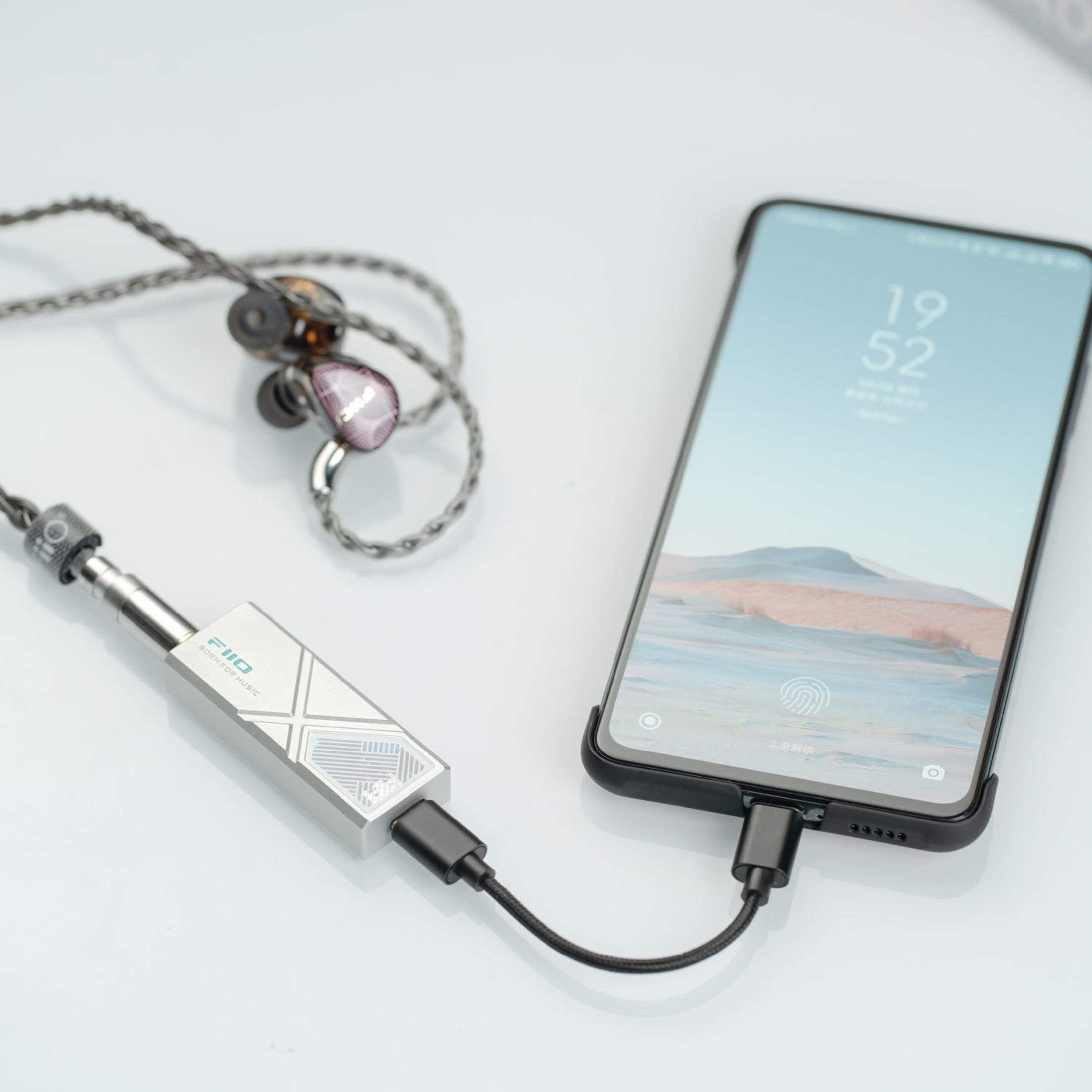 Smartfon podłączony do wzmacniacza FiiO DAC z przewodowymi słuchawkami.