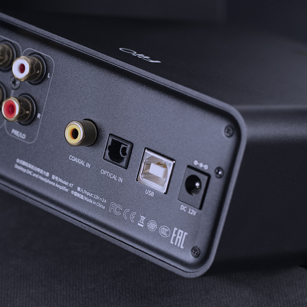 Tylny panel czarnego urządzenia audio z portami RCA, koaksjalnymi, optycznymi, USB i 12V oraz logo certyfikatów.