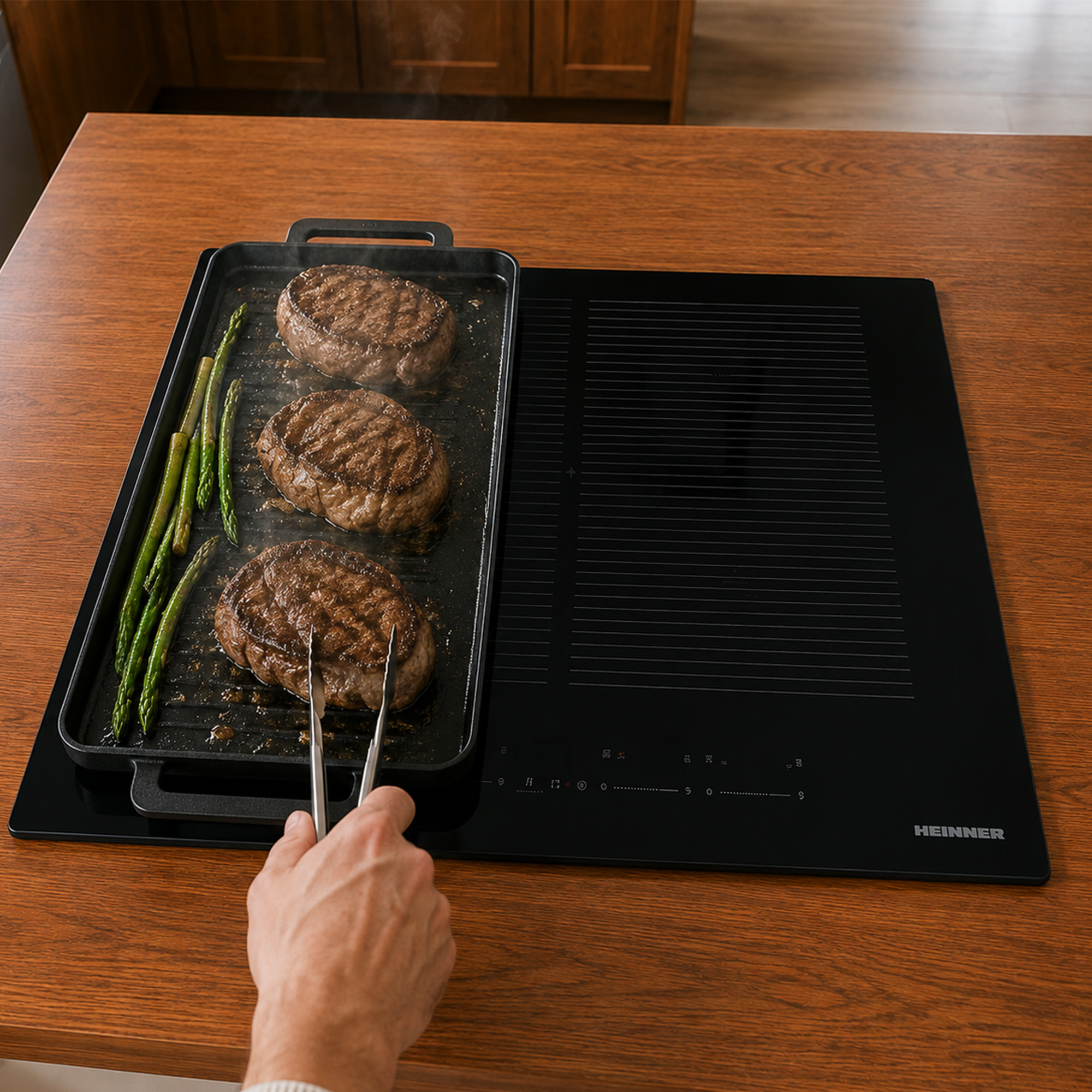Des steaks et des asperges cuisent dans une poêle sur une table de cuisson noire.