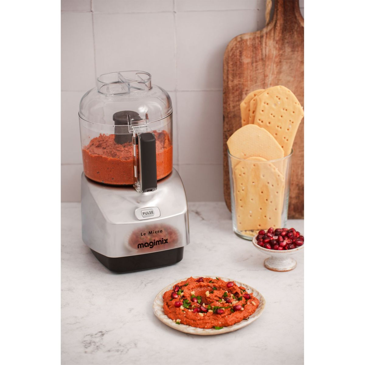 Eine Magimix-Küchenmaschine mit rotem Dip, Crackern, Granatapfelkernen und einer Schüssel mit Dip.