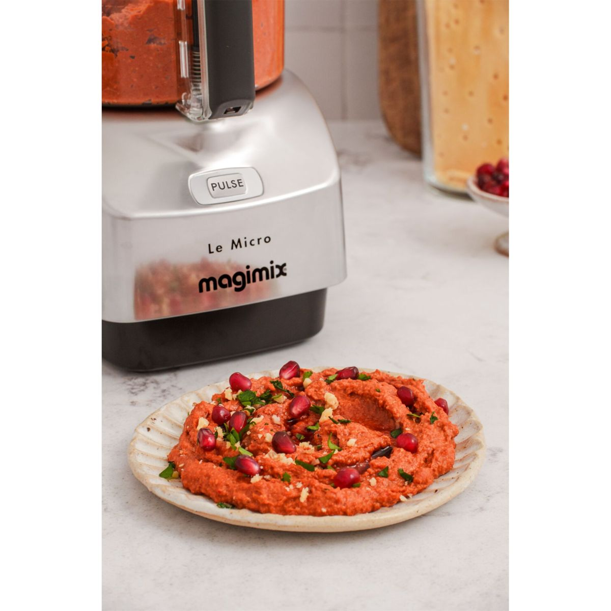 Magimix Le Micro Food Processor neben einem Teller mit rotem Dip, garniert mit Granatapfelkernen und Kräutern.