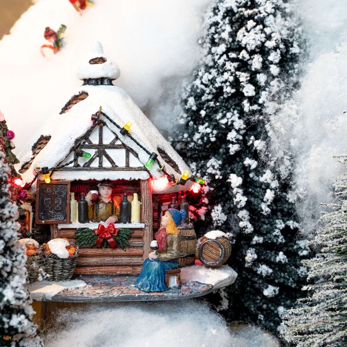Een winters kerstmarktscène met een houten chalet, figuurtjes, wijnvaten en besneeuwde dennenbomen.
