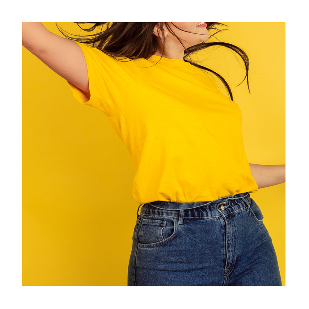 Una mujer con camiseta amarilla y jeans azules baila dinámicamente frente a un fondo amarillo, cabello al aire.