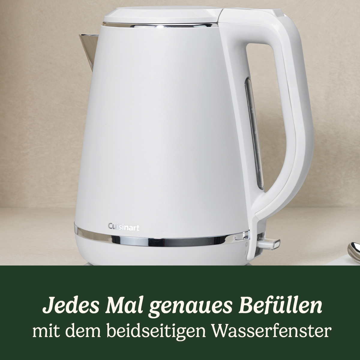 Ein weißer Cuisinart Wasserkocher mit silbernem Rand steht auf einer hellen Arbeitsplatte vor einer beigen Wand.