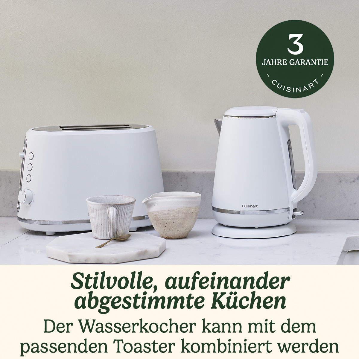 Weißer Toaster und passender Wasserkocher auf einer Marmorarbeitsplatte neben einer Tasse.