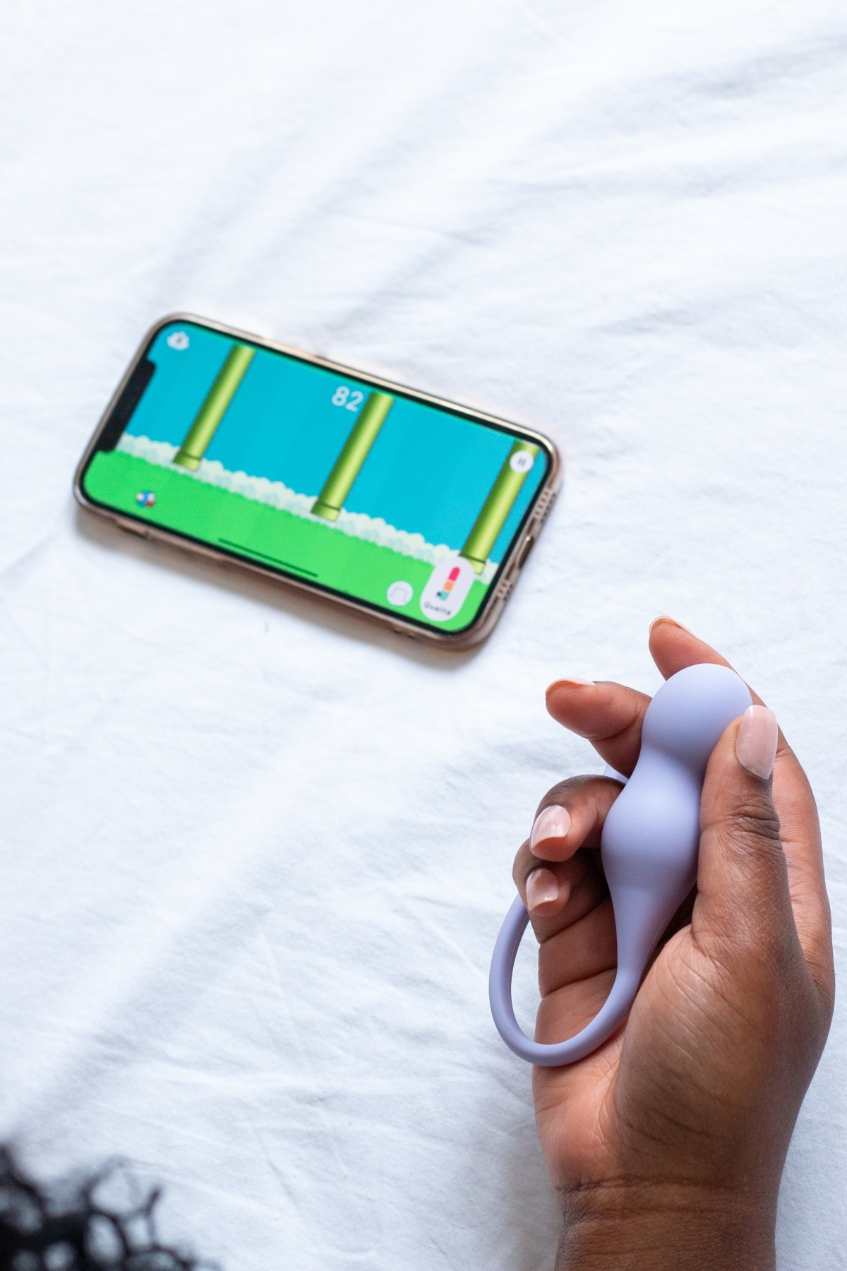 Eine Hand hält ein lila Spielzeug neben einem Handy mit einem Videospiel auf einem weißen Bett.