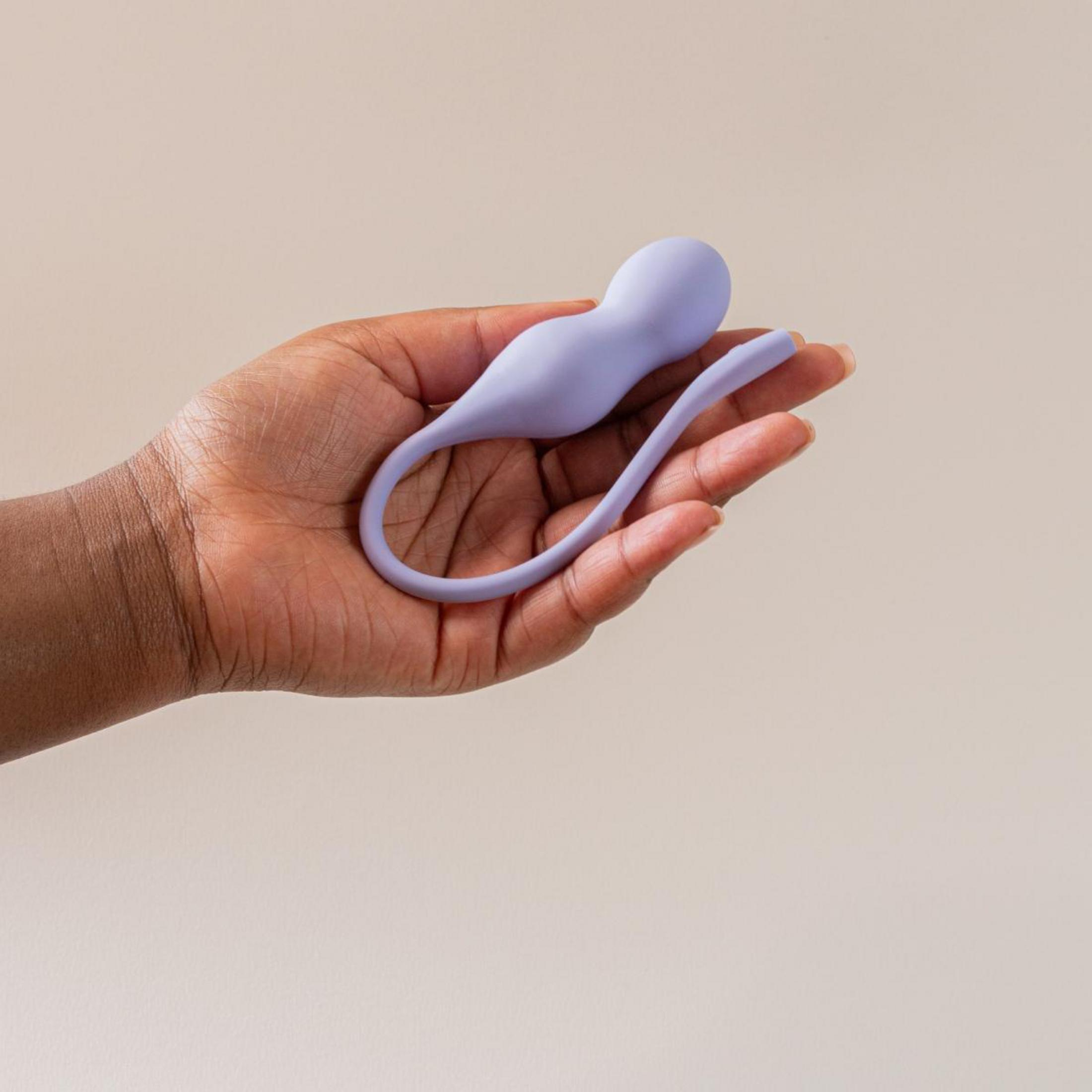 Eine offene Hand hält ein glattes, lila Wellness-Produkt vor einem neutralen Hintergrund.