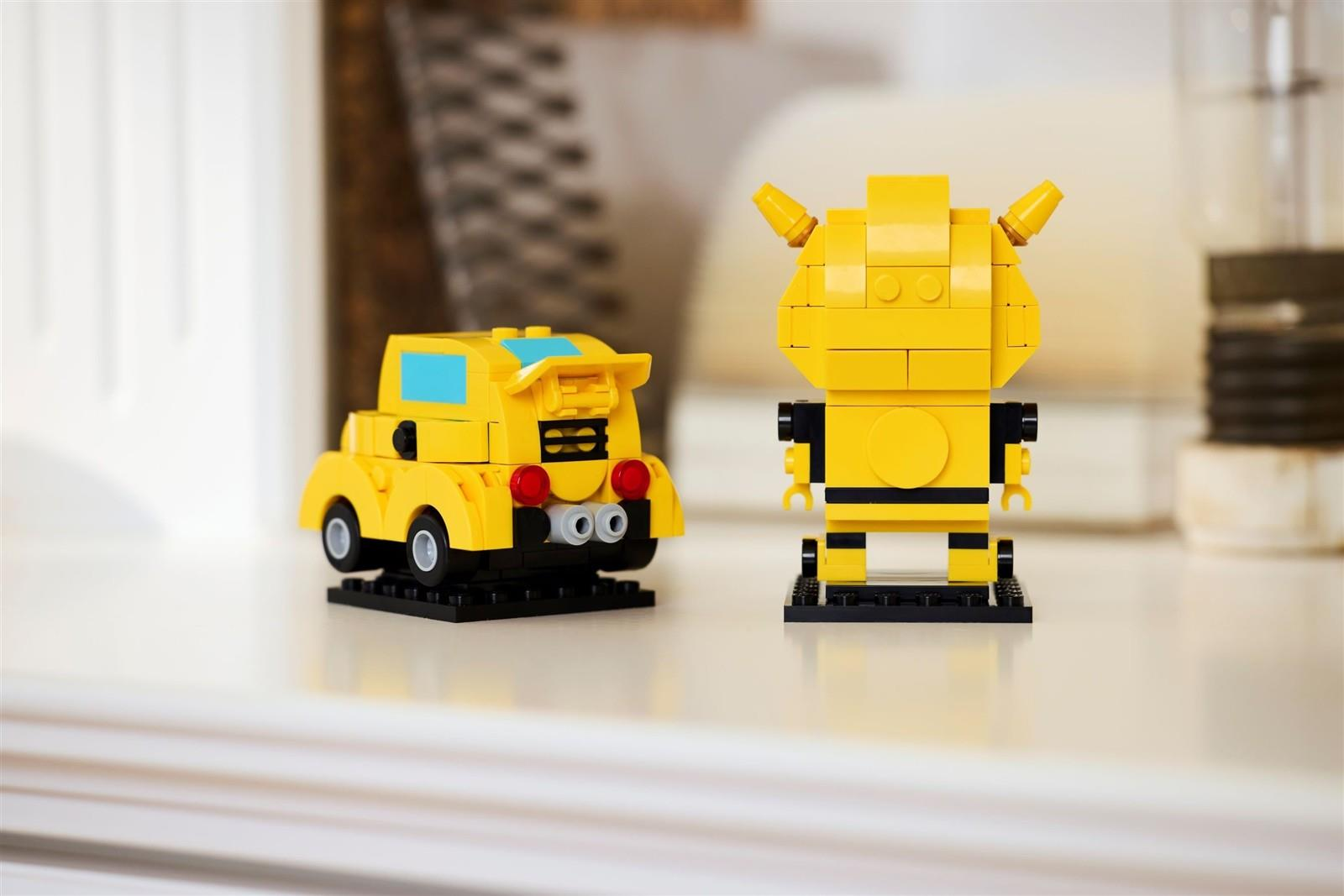 Beyaz bir yüzeyde sarı bir Lego araba ve sarı bir Lego robot yan yana duruyor.