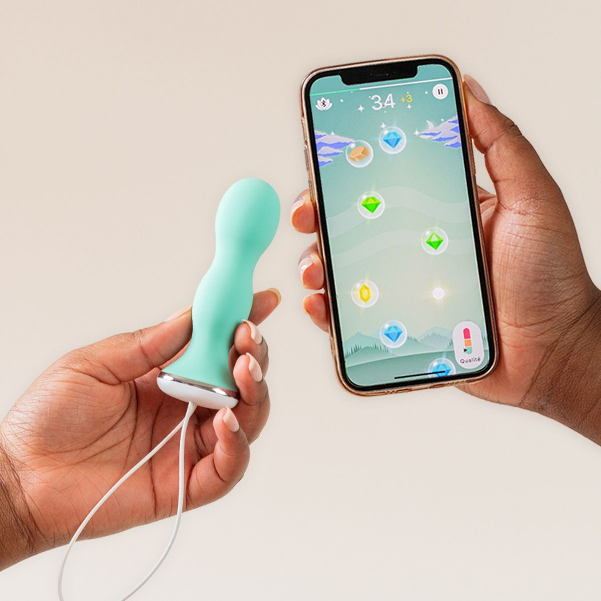 Hände halten ein mintgrünes Sexspielzeug und ein Smartphone mit einer App-Oberfläche auf beigem Hintergrund.