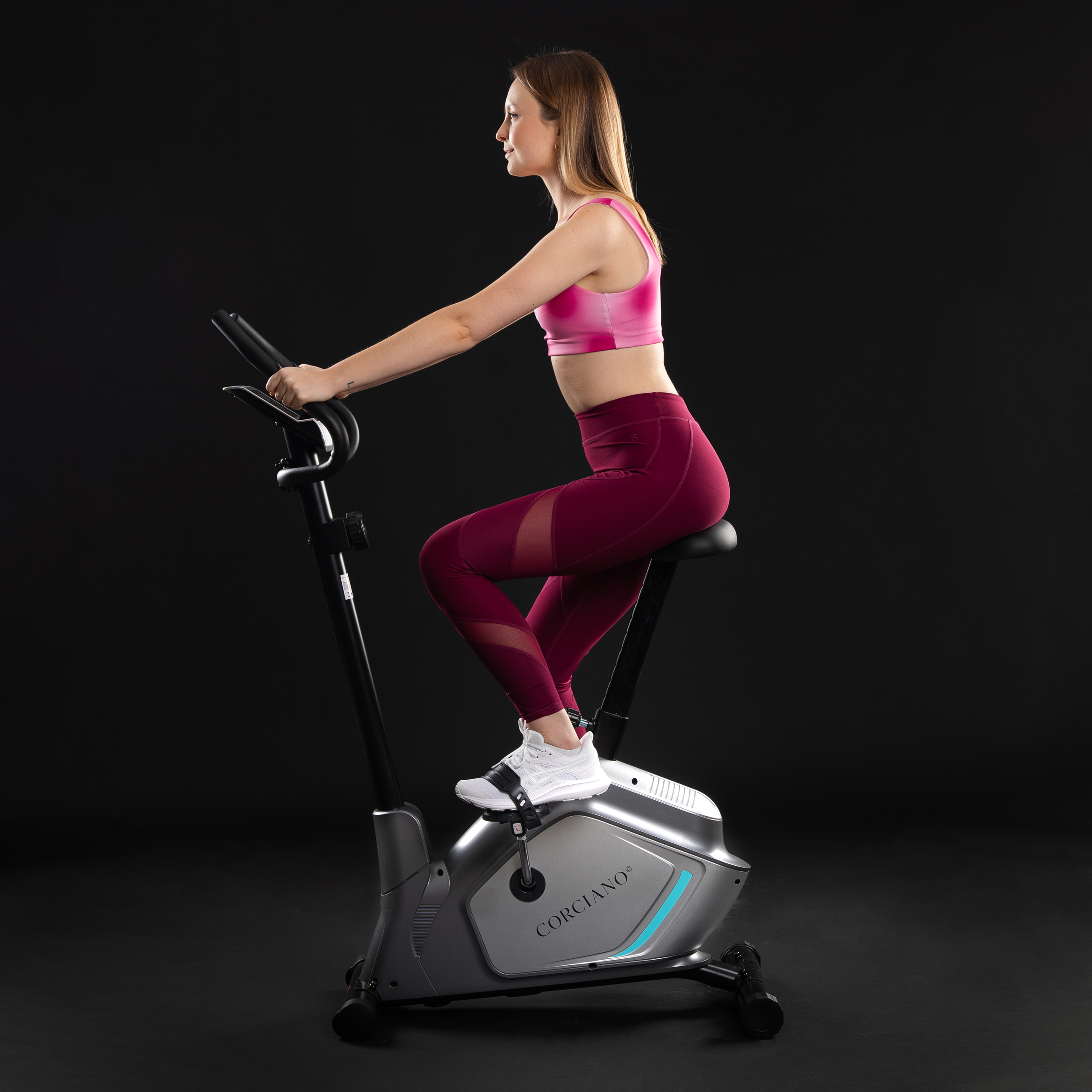 Kobieta w stroju sportowym ćwiczy na rowerku stacjonarnym na czarnym tle.