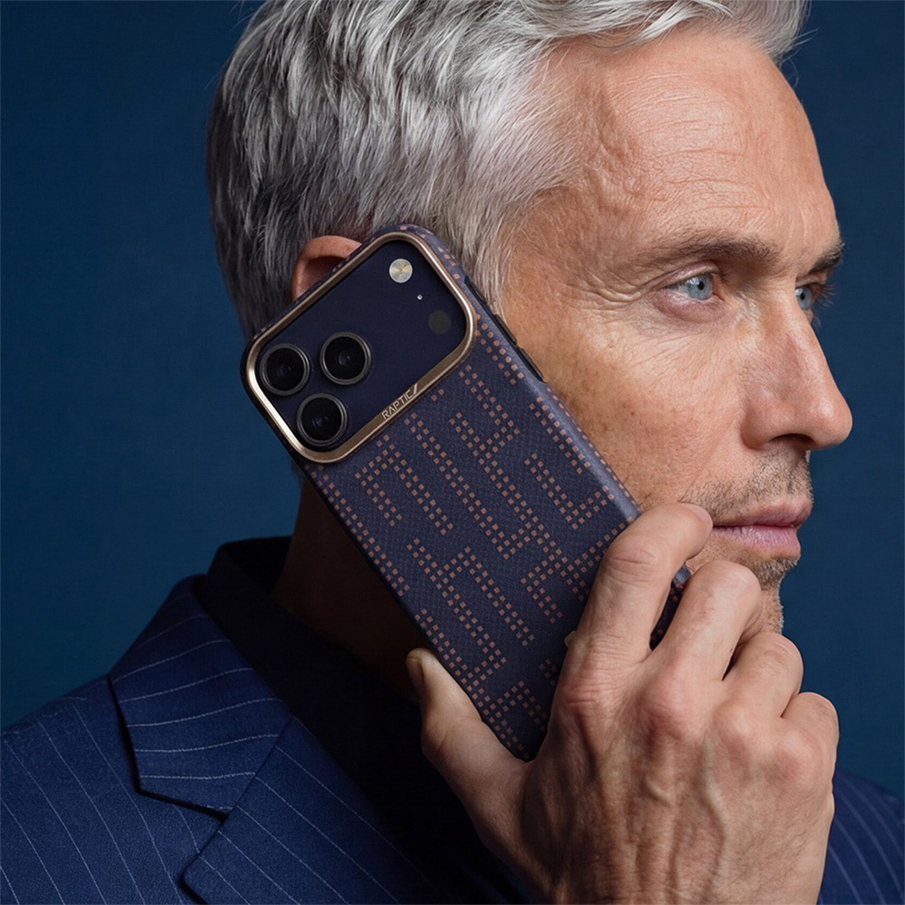 Un hombre con canas sostiene un teléfono inteligente con funda oscura texturizada contra un fondo azul.