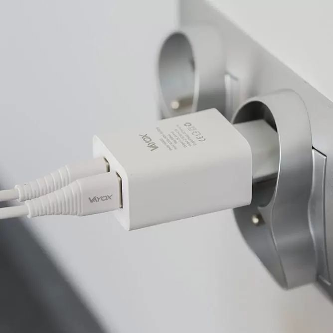 Egy fehér Vayox USB töltő két fehér kábellel bedugva a fali aljzatba.