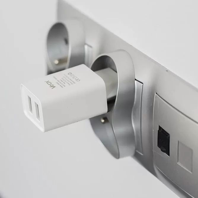 Egy fehér USB-töltő modern ezüst fali aljzatba dugva fehér fal előtt.