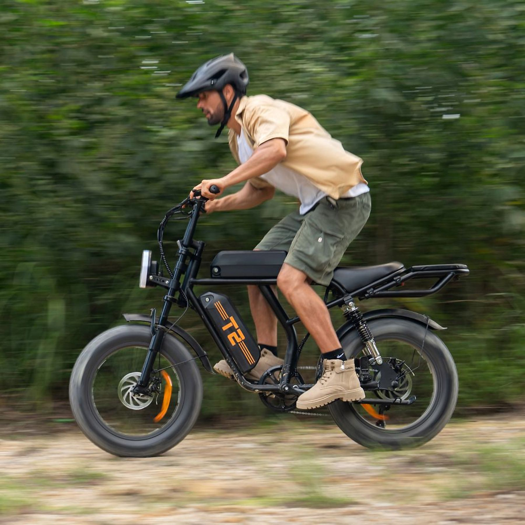 Ein Mann fährt auf einem mattschwarzen E-Bike mit dicken Reifen über einen von Grün umgebenen Feldweg.
