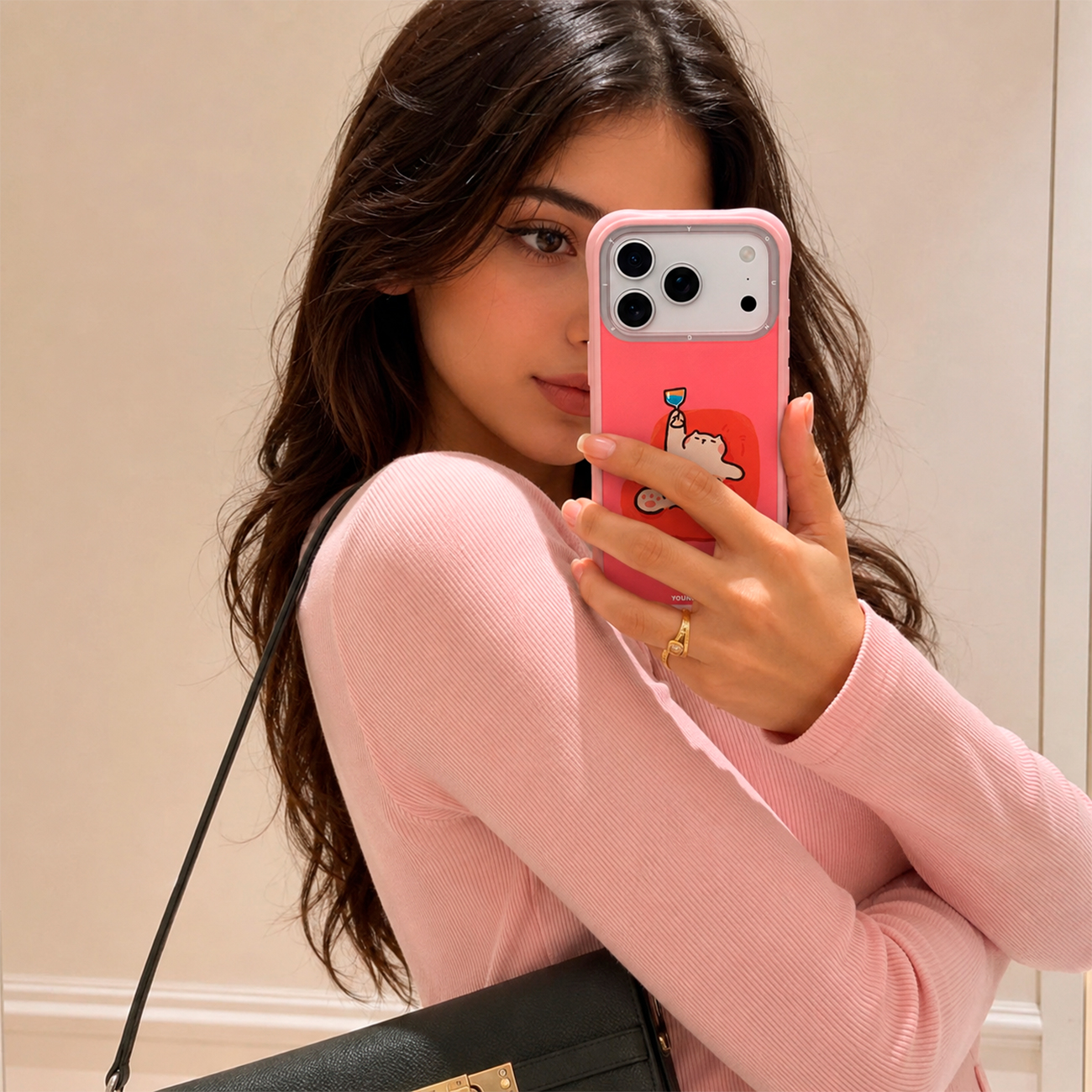 Una castaña con una camiseta rosa se hace un selfi frente al espejo con un teléfono rosa.