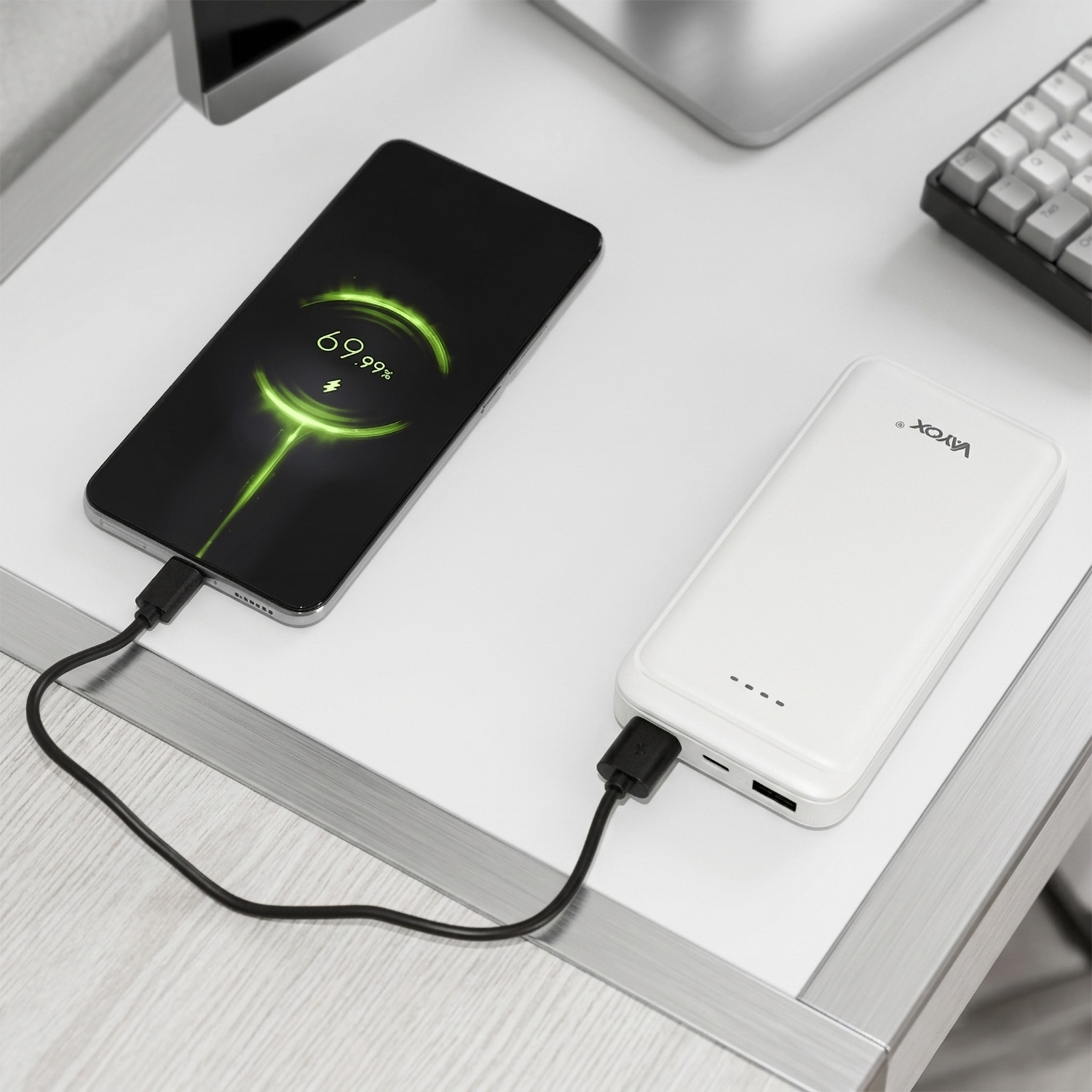Smartfon ładuje się na biurku z powerbanku za pomocą czarnego kabla.