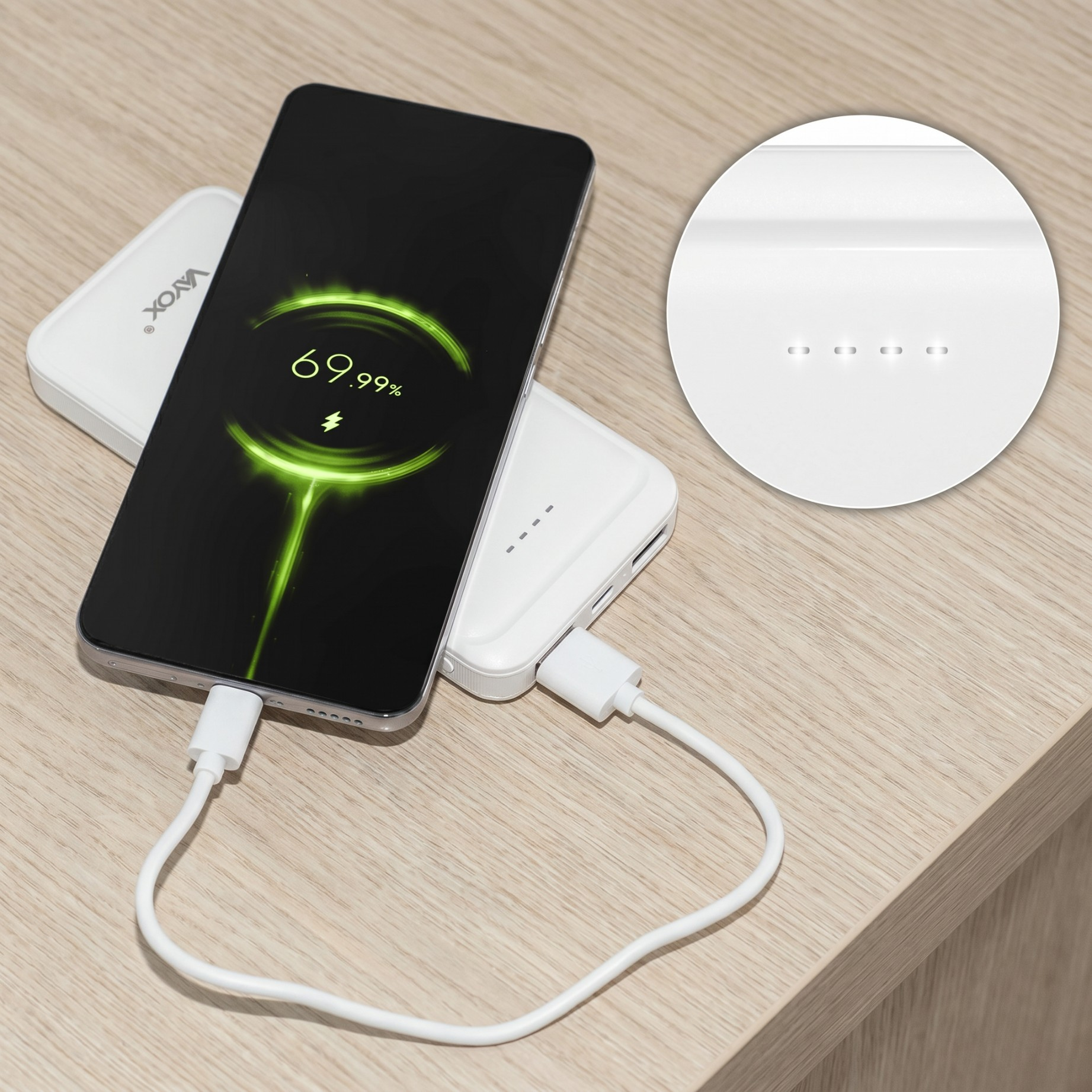 Smartfon ładuje się z białego powerbanka za pomocą kabla na drewnianym blacie.
