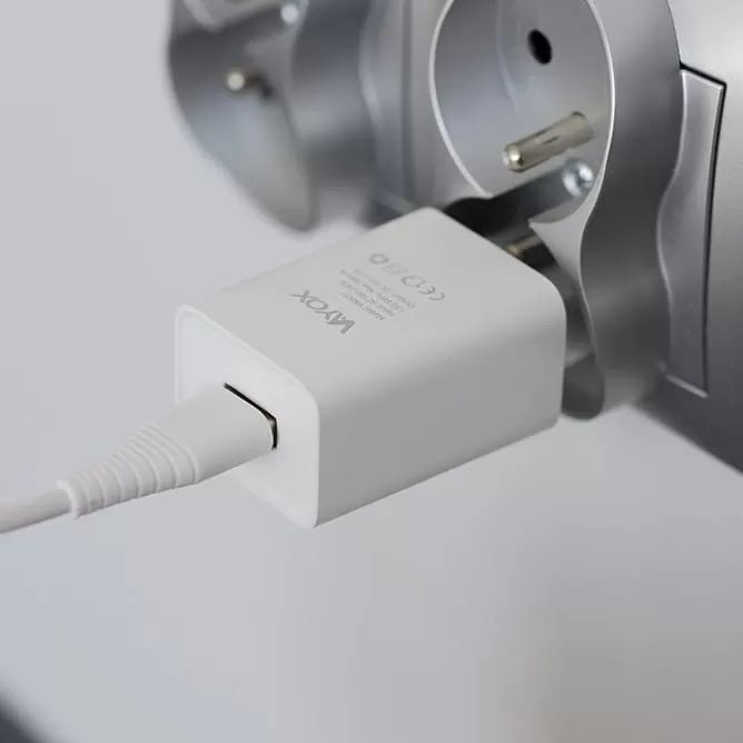 Egy fehér töltőkábel van bedugva egy hálózati adapterbe, amely a fali aljzatba csatlakozik.