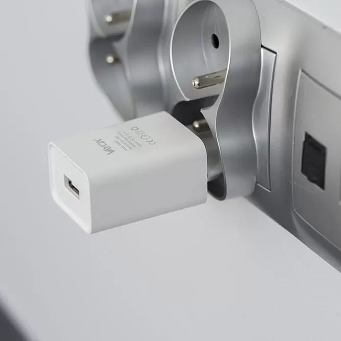 Egy fehér USB töltő csatlakozik egy falra szerelt szürke elosztóba.